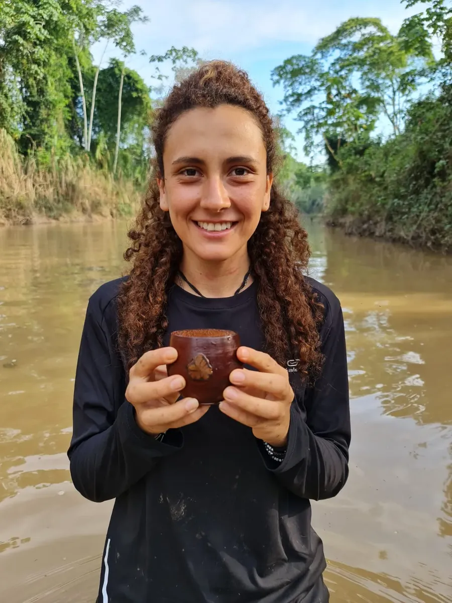 Participante sonriente con un cuenco entre las manos, a la orilla de un río